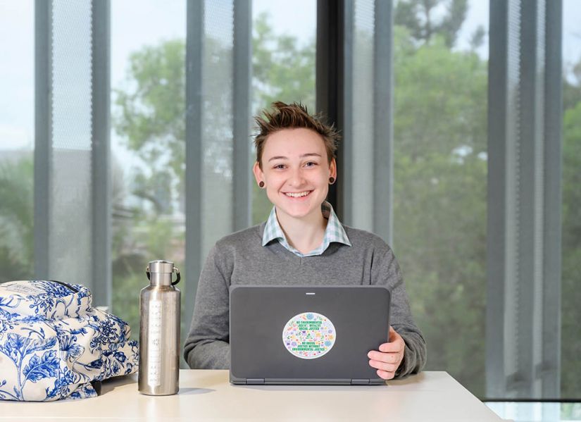 Smiling student sits in front of a laptop.