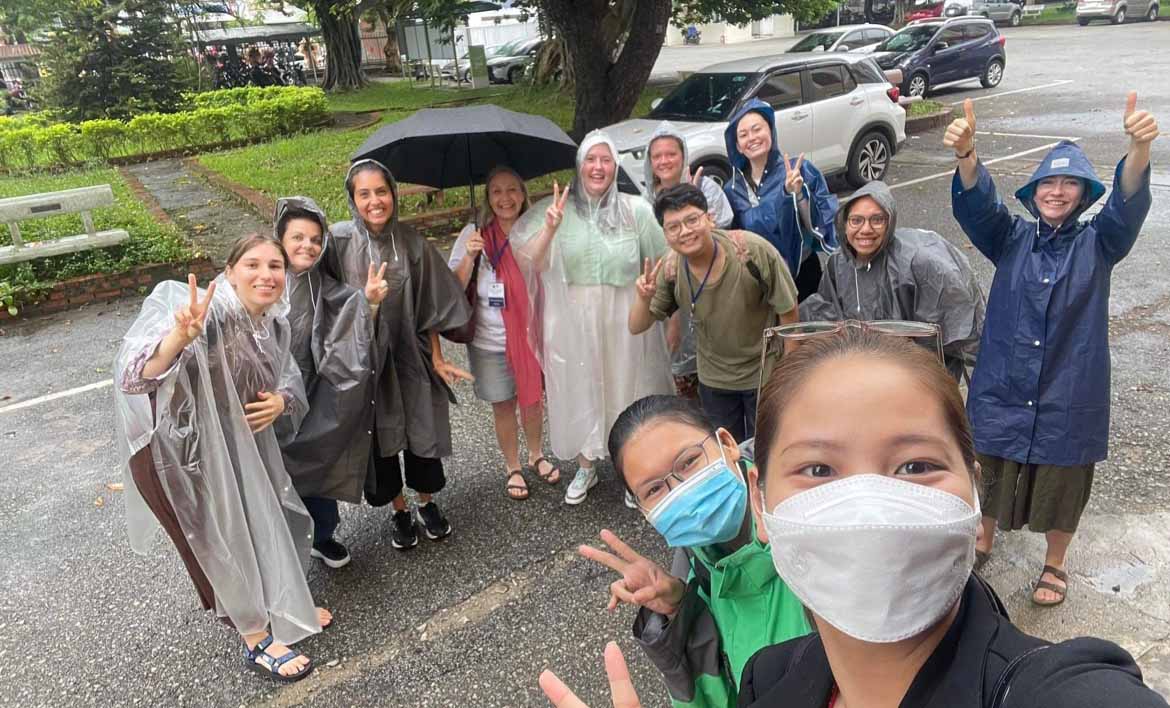 Soaking wet and laughing after being hit by a burst of rain a group of Australian and Vietnamese students wave at the camera.