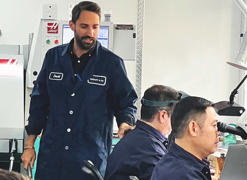 David Barker is in a full body blue jumpsuit standing, while two of his team are sitting around the same area.