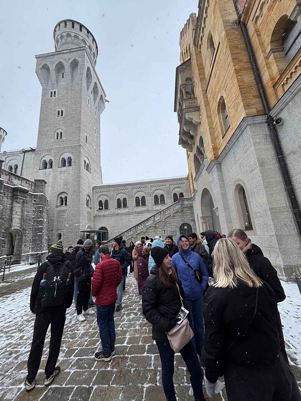 A group of students stand in front of a university building that looks like a stone tower of a medieval castle.