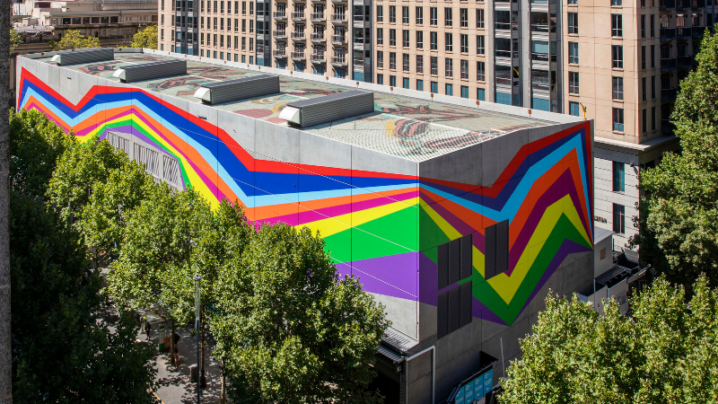 An arial image of a concrete building with a colourful abstract artwork across the outside facade