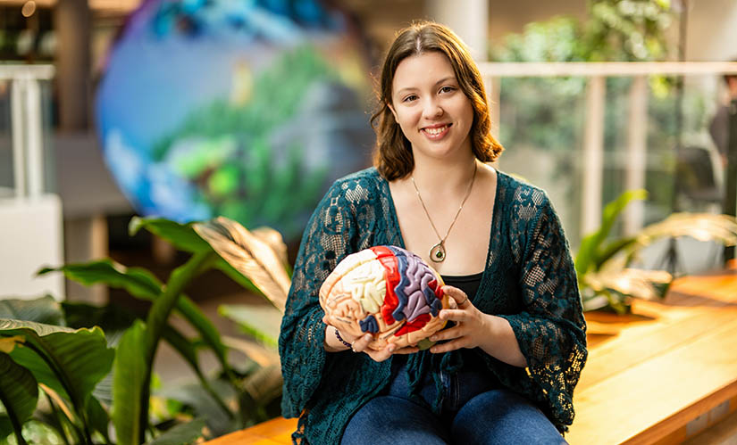 A young female student sits at a bench looking at a model of a brain.