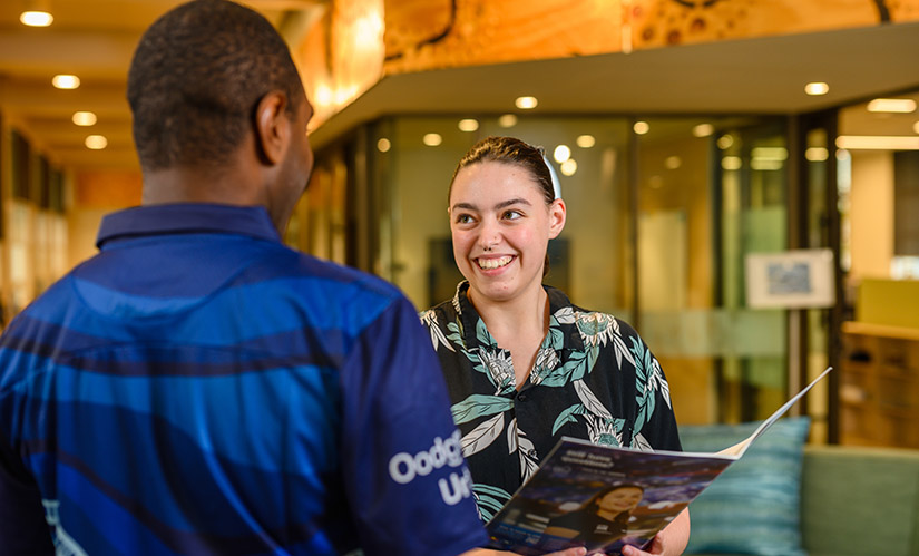 A male staff member in an Oodgeroo Unit shirt helps a female student.