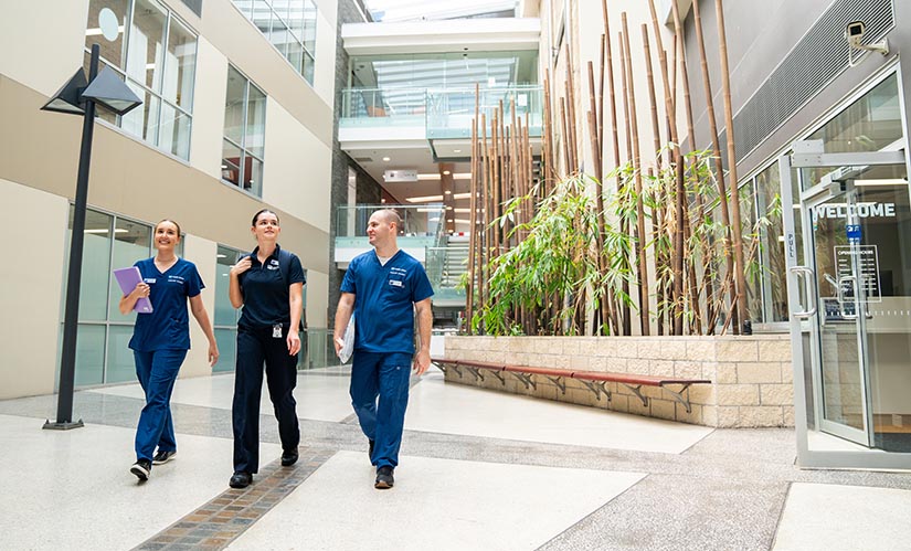 Three students in clinical uniforms walk through the lobby of the QUT Health Clinics.