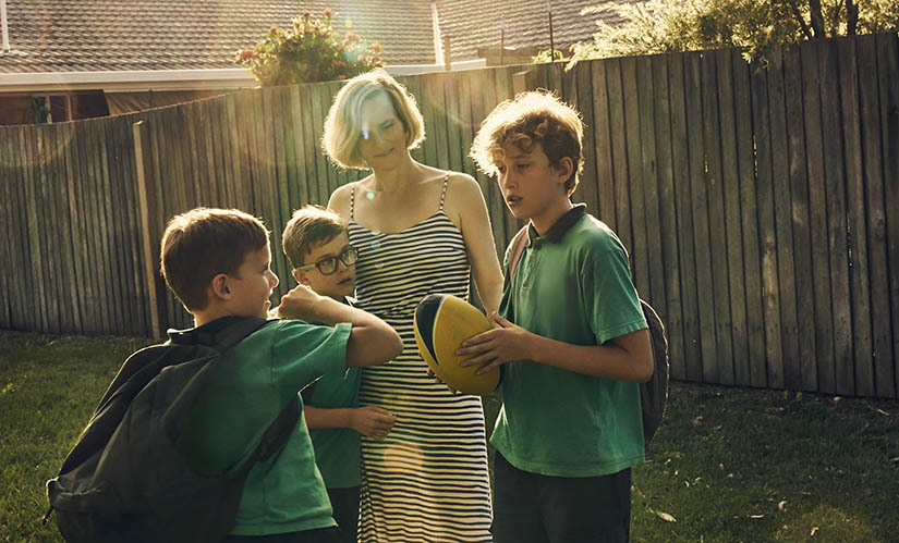 A mother and three boys in school uniforms stand in a backyard.