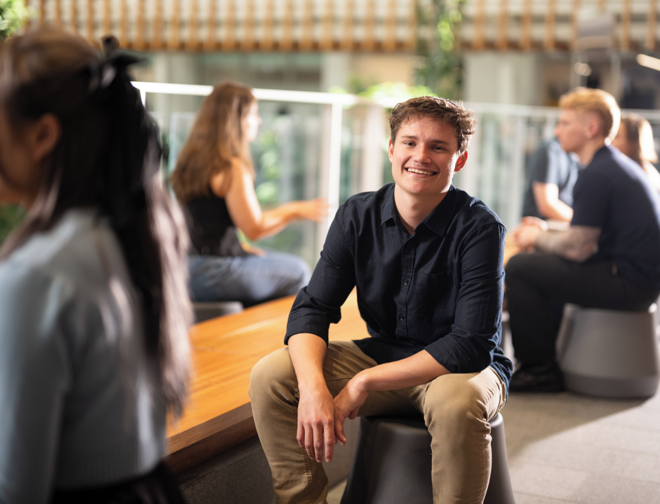 Student sitting on stool, smiling at the camera 