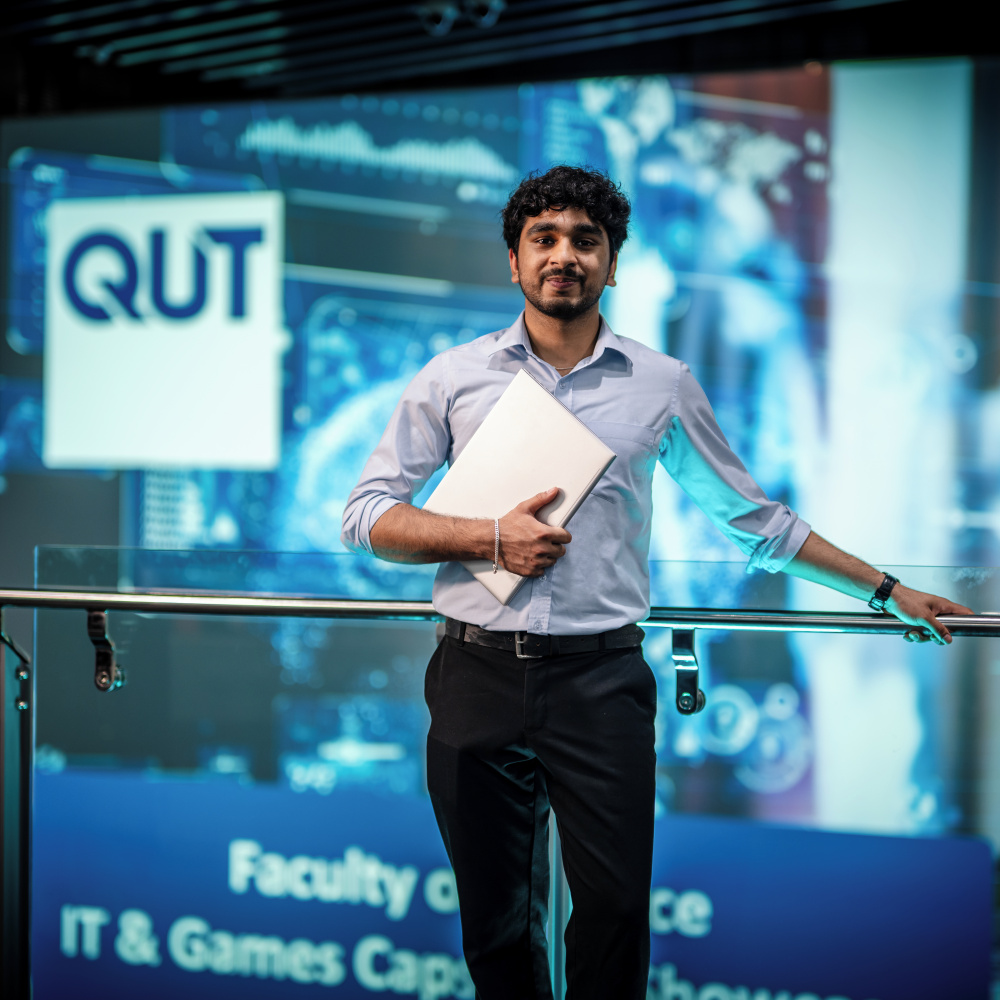 Agam Sood standing holding a laptop in front of The Cube digital screen