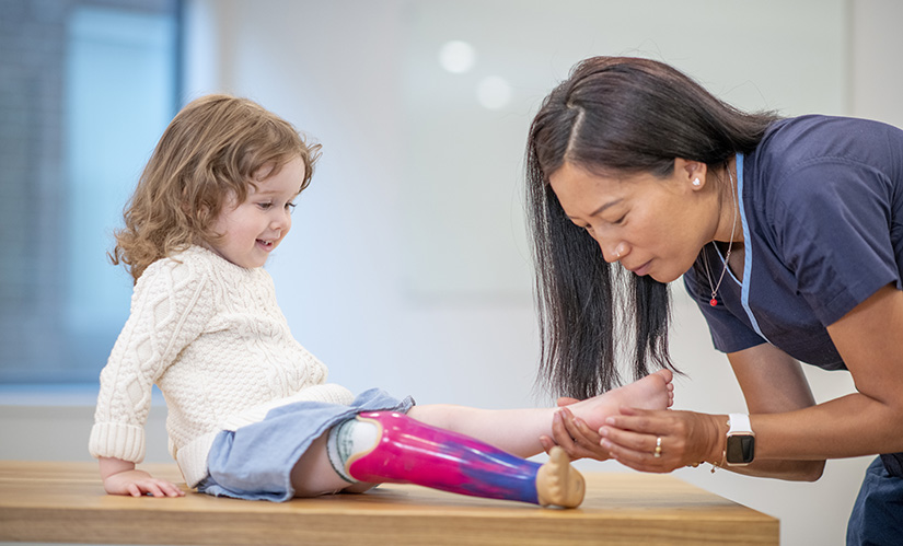A female podiatrist wearing scrubs performs a foot exam on a young girl.