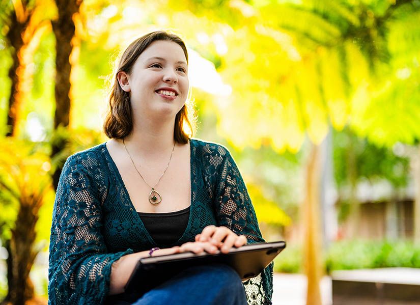 A female student looking happy and relaxed with a laptop on campus.