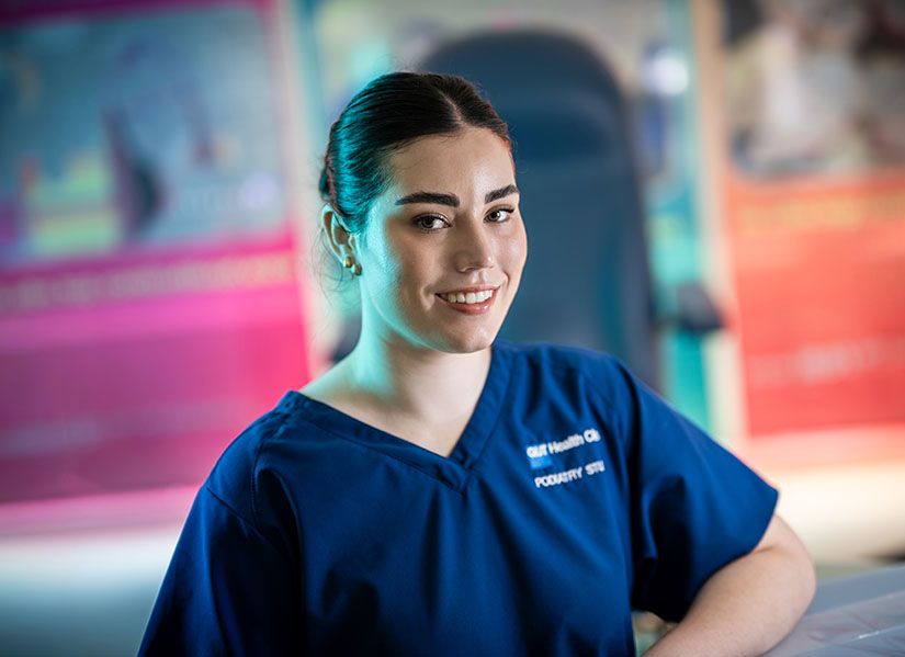 A female student in blue scrubs sits in a podiatry clinic.