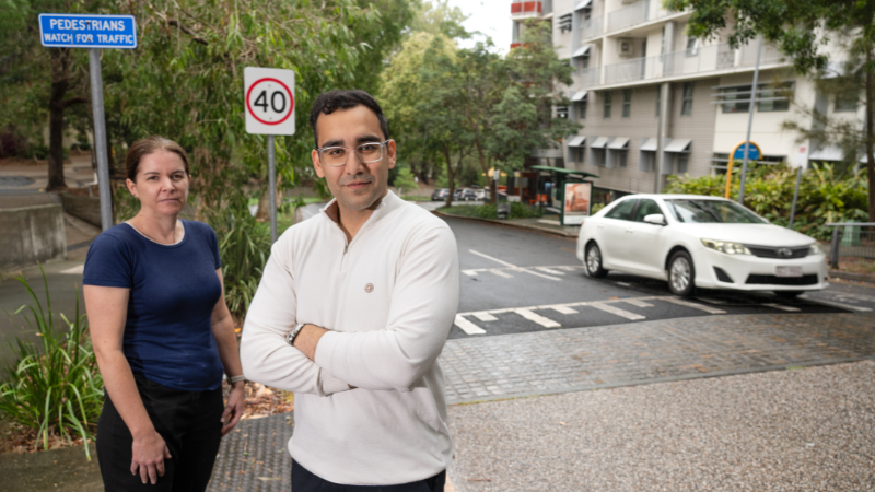 Two researchers stand next to a road where I white car is driving.