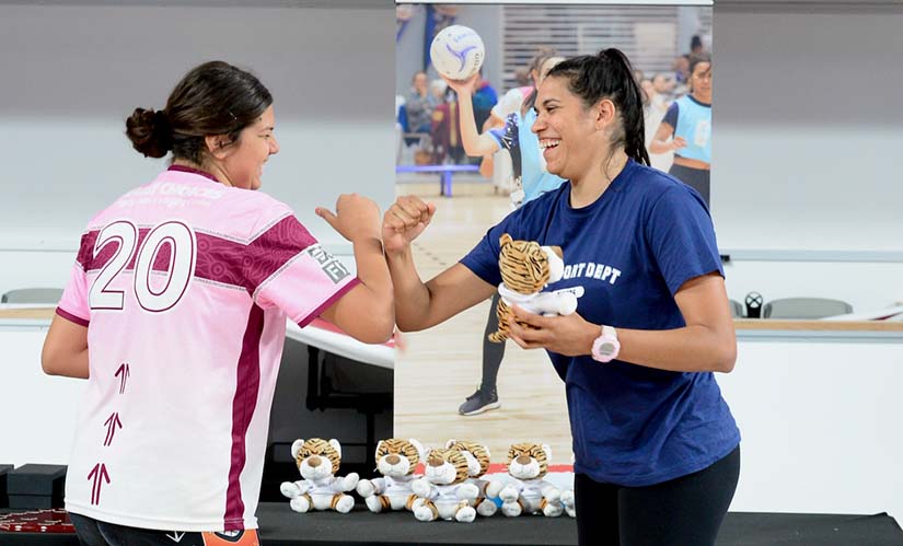 Awards ceremony for the Deadly Choices Murri Netball Carnival, a female student smiles as she hands a prize to a player.