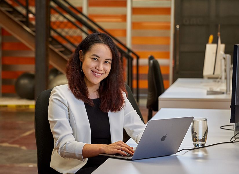 Executive MBA graduate, Angel Chan, sitting at a desk working on her laptop.