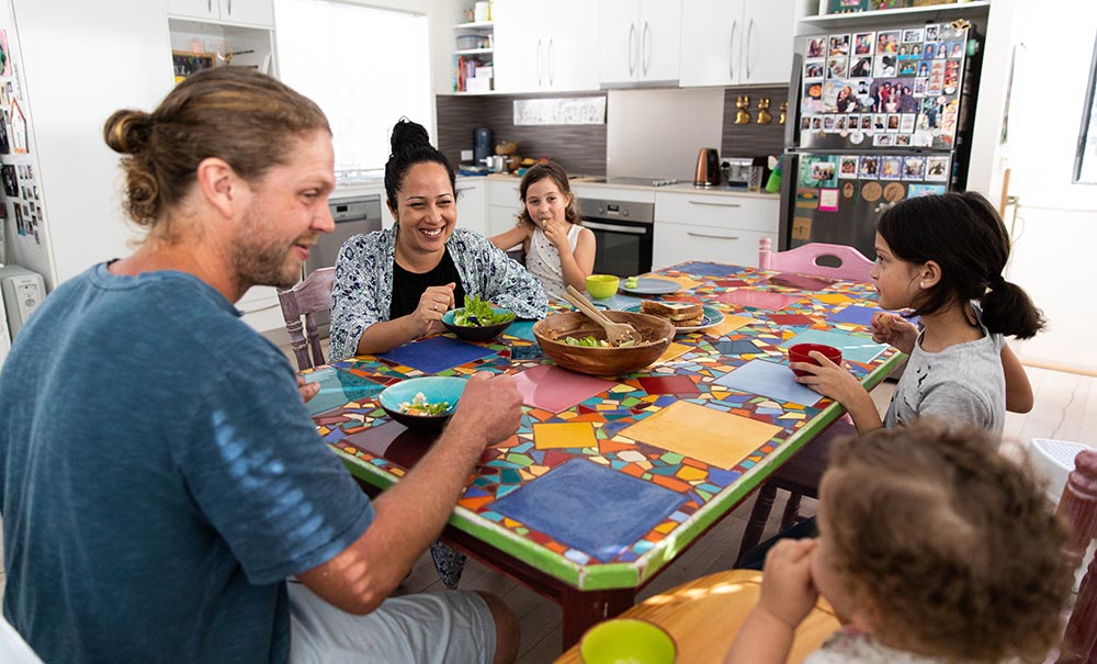 A mum a dad and three kids sit around a brightly tiled mosaic kitchen table.