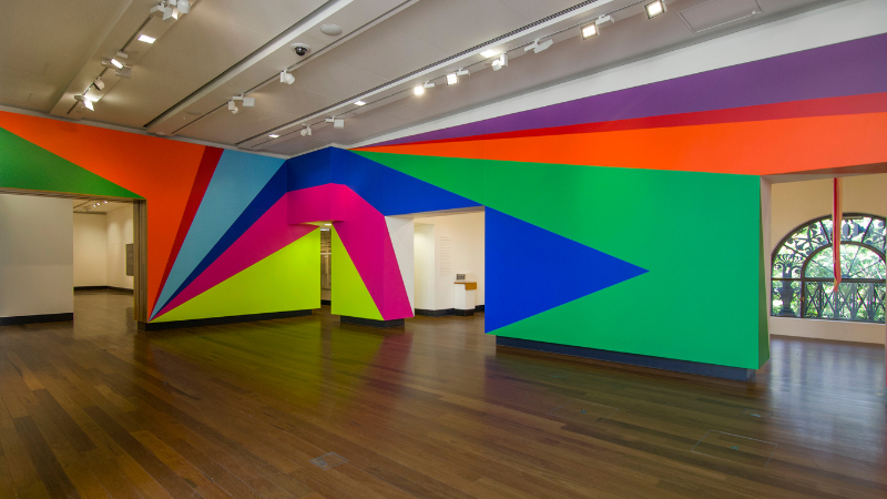 A room with white walls and a colourful abstract installation painted across it of diagnoal colours.