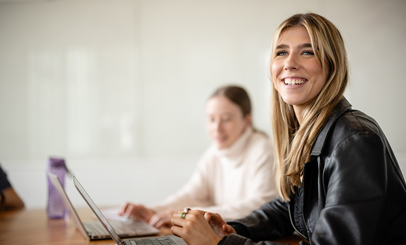 A young woman sits at a desk with a laptop open infront of her.