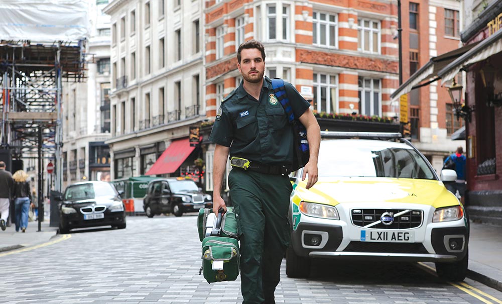 A male paramedic in London walks with purpose from his vehicle.