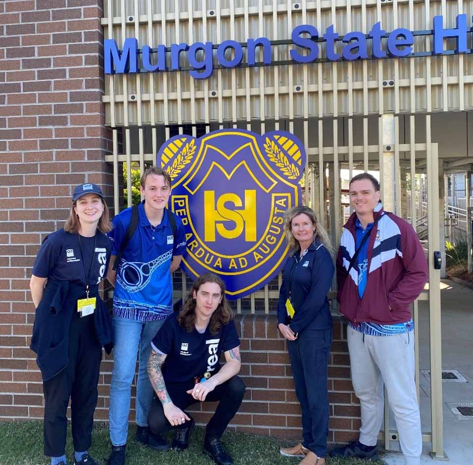 A group of uni students and lecturer Joanne Voisey stand in front of the gates of Murgon State High School.