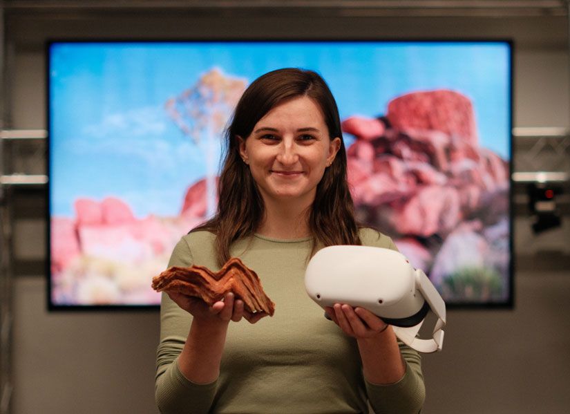 Image of PHD student Cael Gallagher holding a VR headset and a rock formation