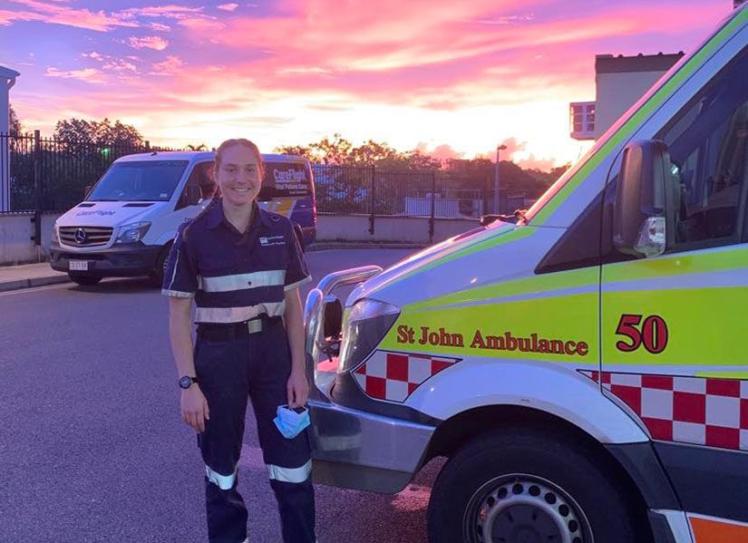 Woman in paramedic uniform stands next to ambulance