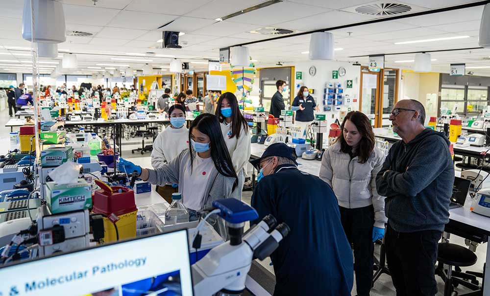 A group of students in a laboratory, supervised by a QUT academic, use a pipette to pipe liquid from a beaker to a flask.