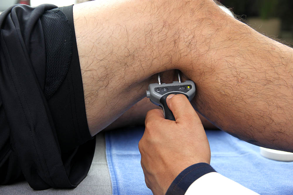 A clinician holds a device with two metal prongs against the bare leg of a test subject.