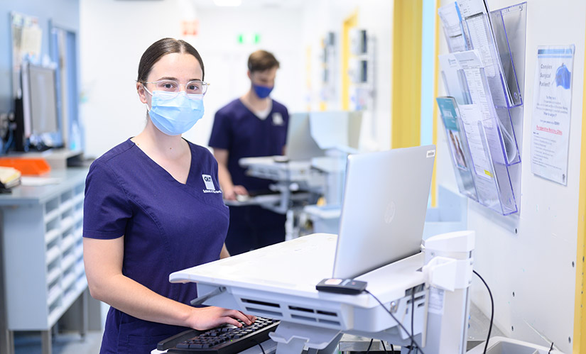 Nursing student stands in front of a computer while on placement in a hospital.