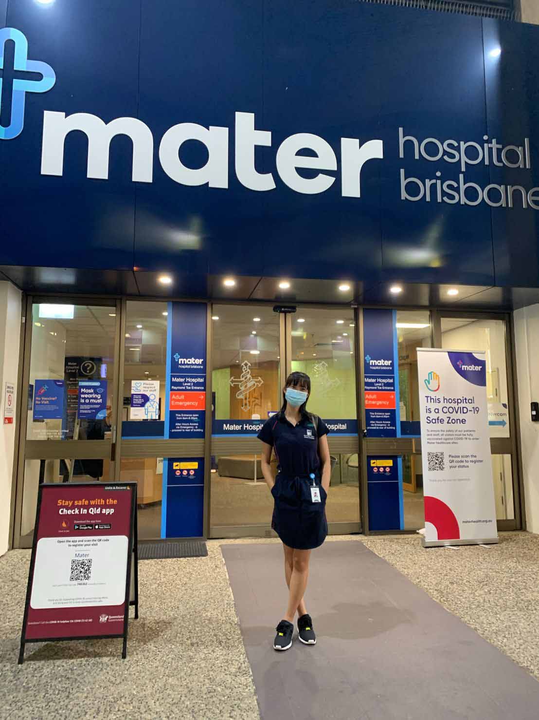 A woman in clinical uniform standing in a hospital foyer.