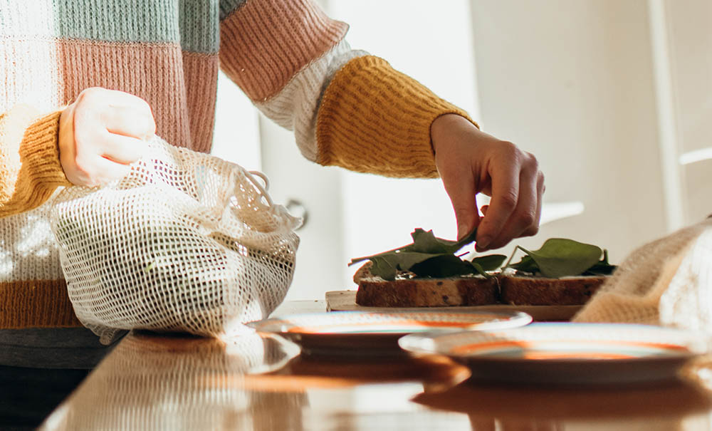 A student in a thrifted jumper is making a sandwich, carefully placing baby spinach leaves on sliced bread.