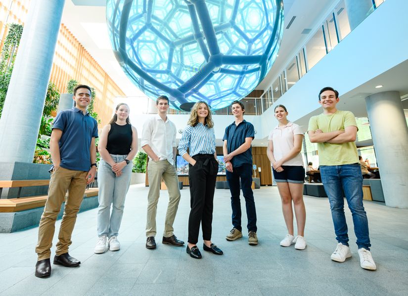 Seven confident QUT student standing under a large digital sphere.