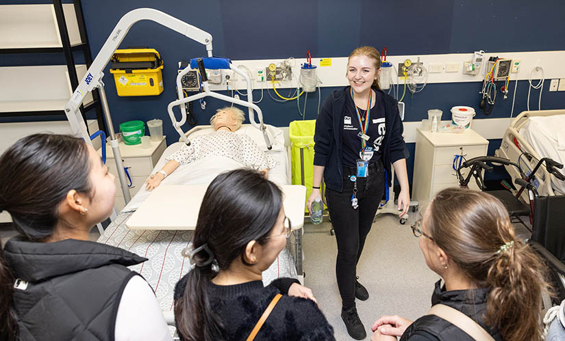 A current nursing student demonstrates how students learn using interactive, life-sized human dummies in hospital beds.
