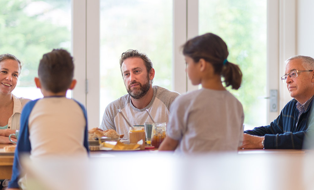 A father and a grandfather listen as two children tell a story at the dinner table.