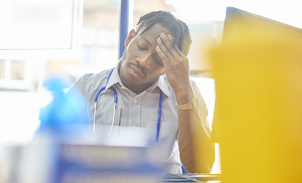 A young, male health student is on clinical placement. He looks tired and is rubbing his forehead.