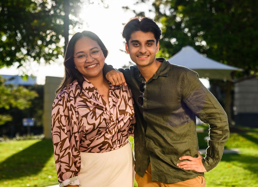 QUT students Sameel Deoji and Judichan (Judi) Kuhn smiling towards the camera at dusk on campus