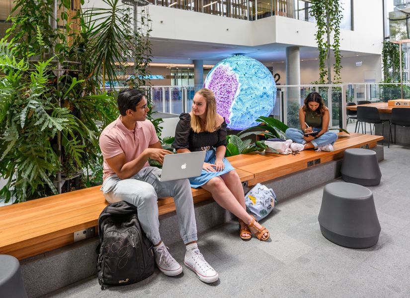 Three Q-U-T students studying on campus in a lush modern building.