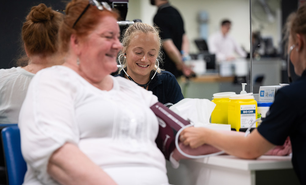 A female student concentrates as the takes the blood pressure of her client.