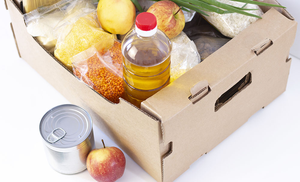 A cardboard box filled with a mix of vegetables, canned food and a bottle of oil.