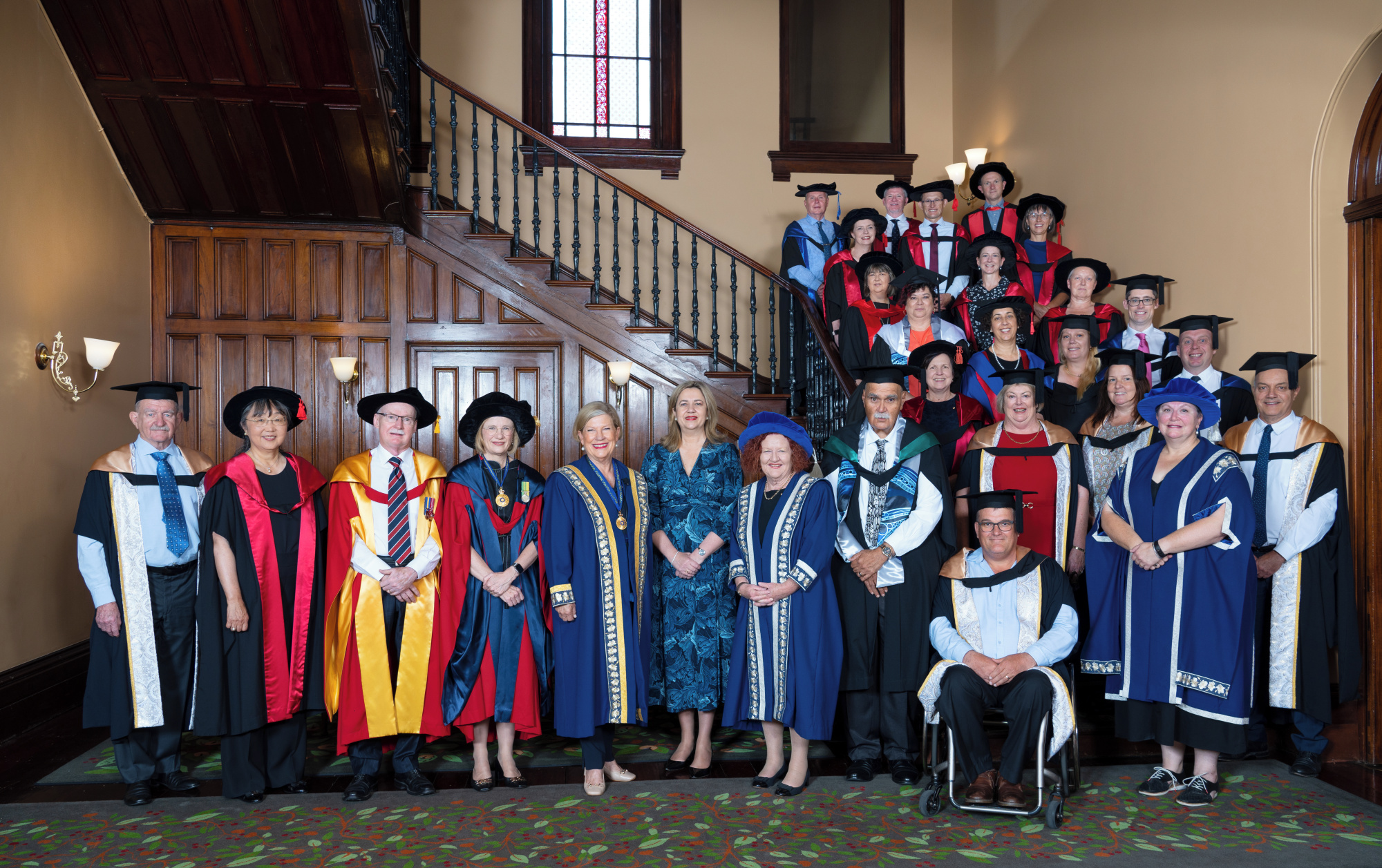 Academics in gowns stand in front of a staircase