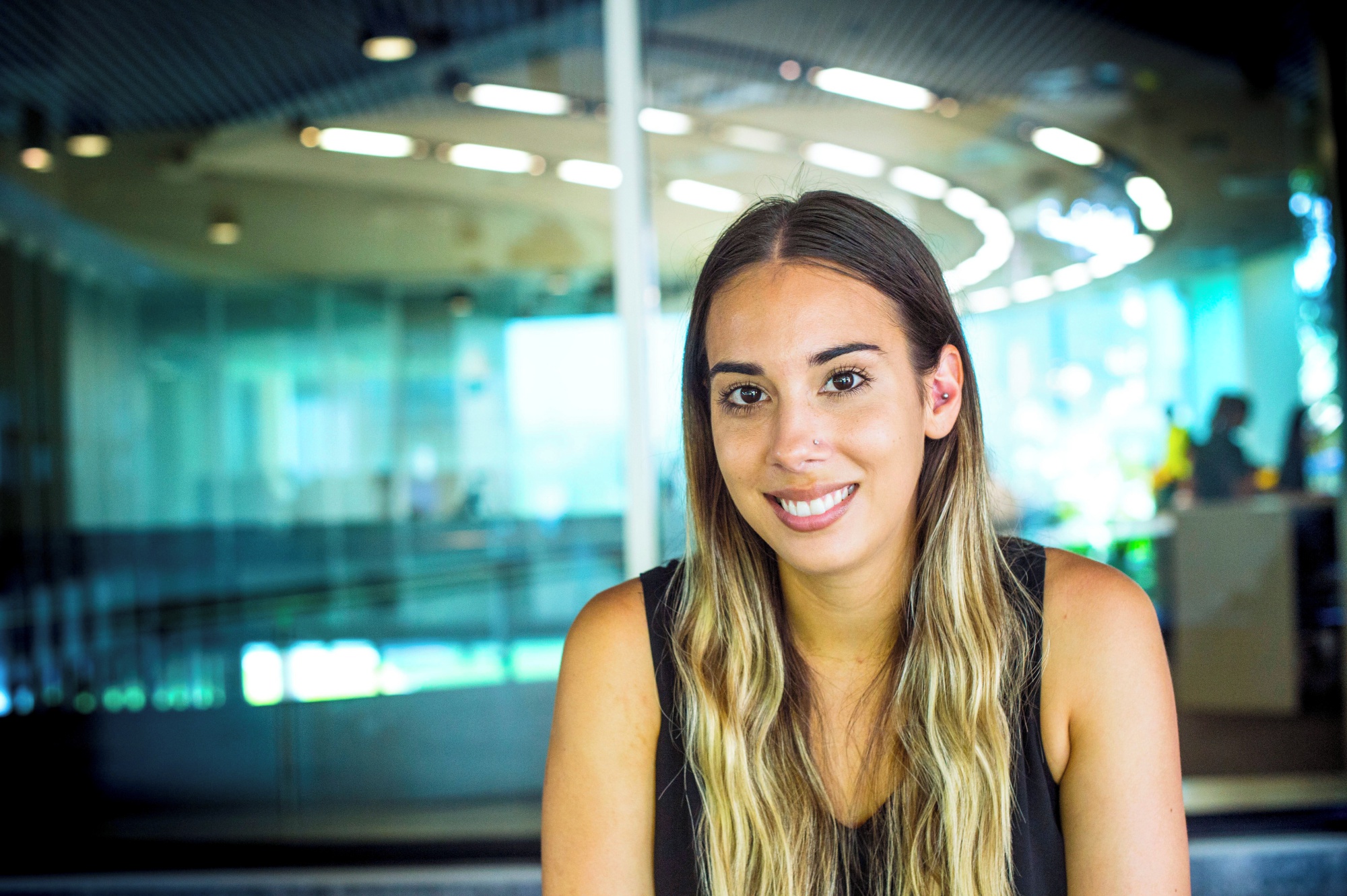 woman with long hair smiles at the camera in front of a glass void filled with lights