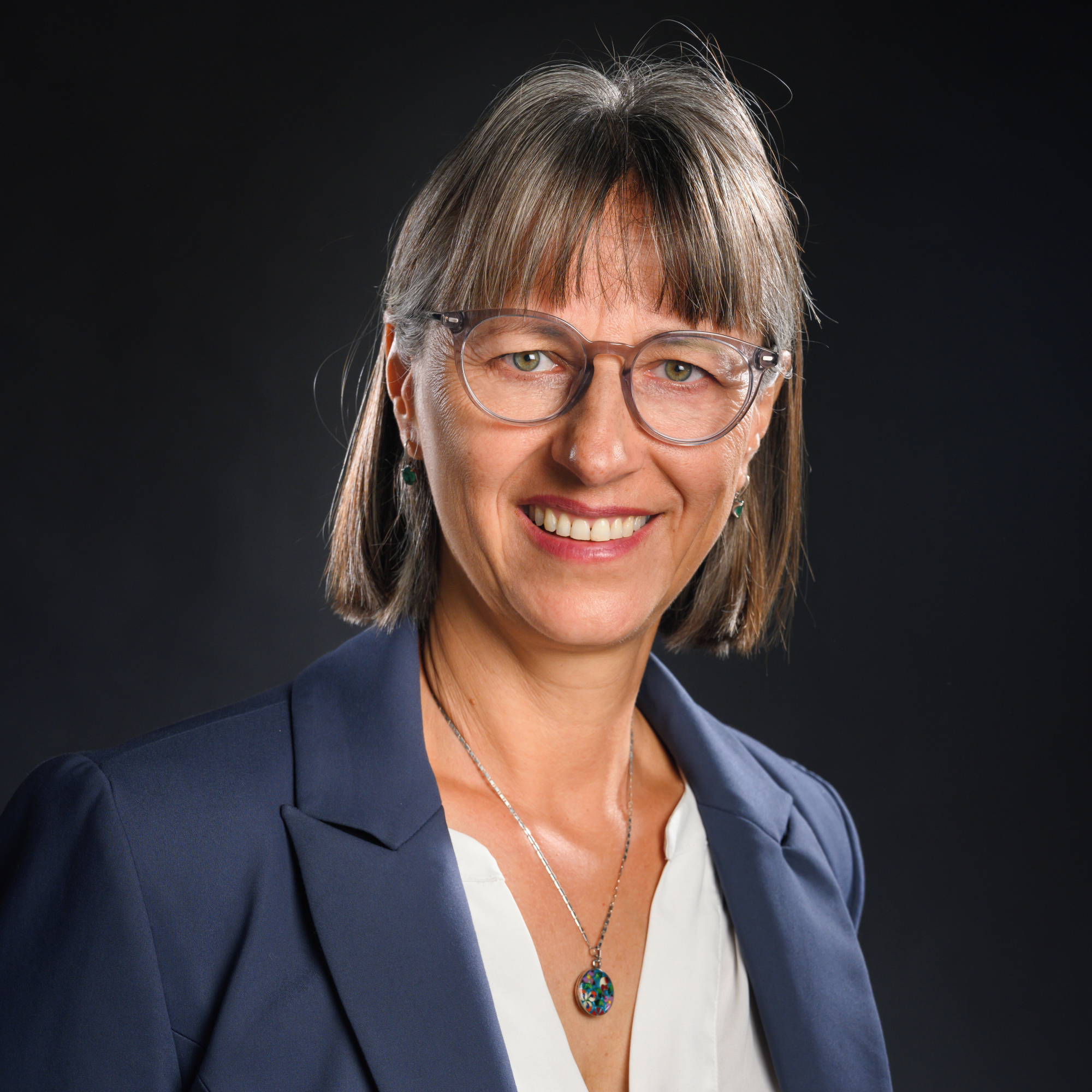 woman wearing glasses and a blue jacket and white blouse smiles at the camera