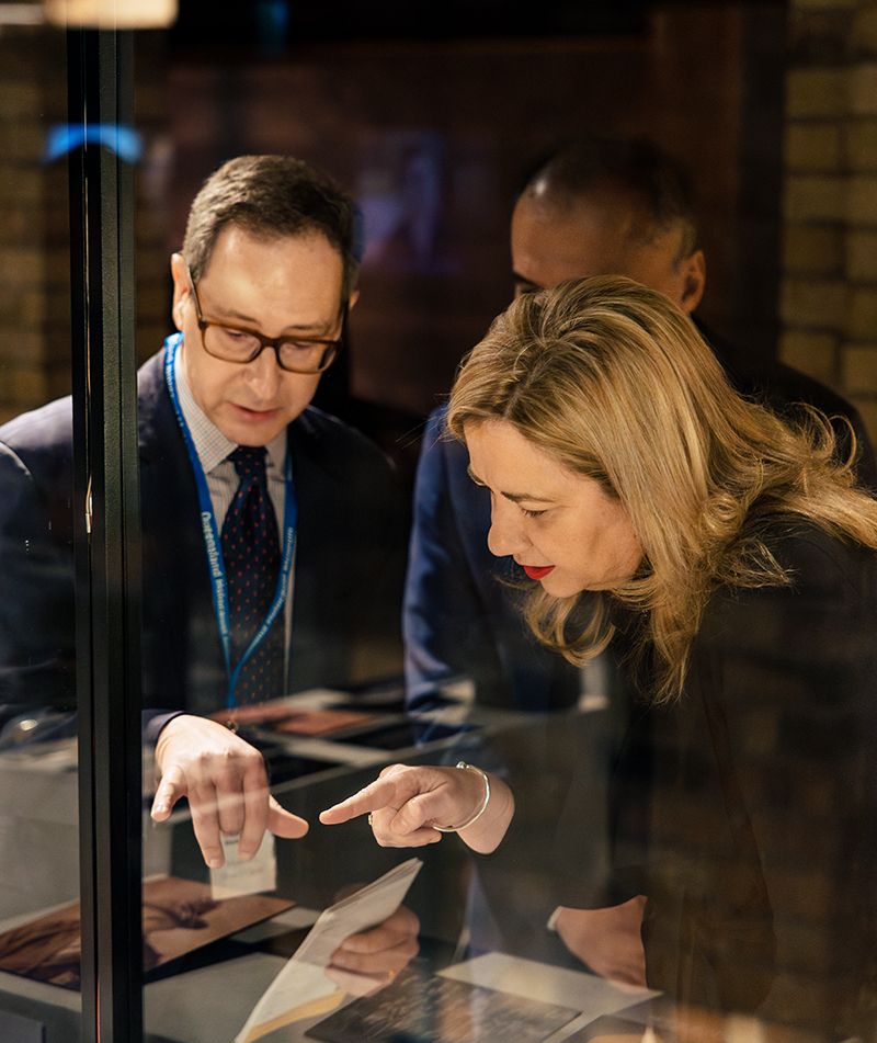 Man in glasses shows woman with blonde hair a museum display in a glass case